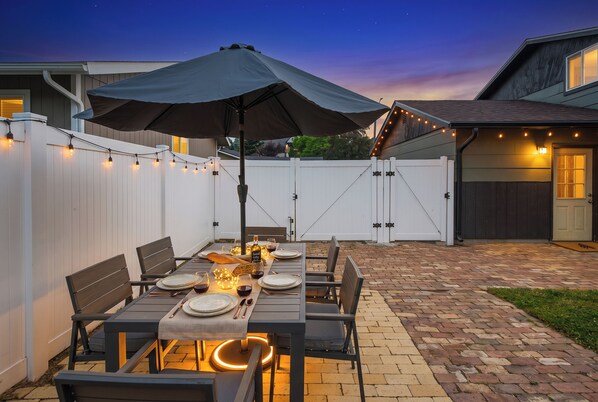 En udendørs terrasse med et spisebord, omgivet af stole og en parasol.