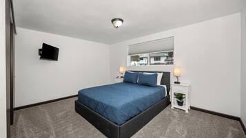 A hotel room with a bed, a television, a nightstand with a lamp, and a window with a view of the outside.