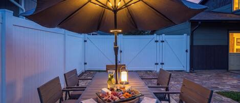 Eine Terrasse im Freien mit Esstisch, Sonnenschirm und Laterne.