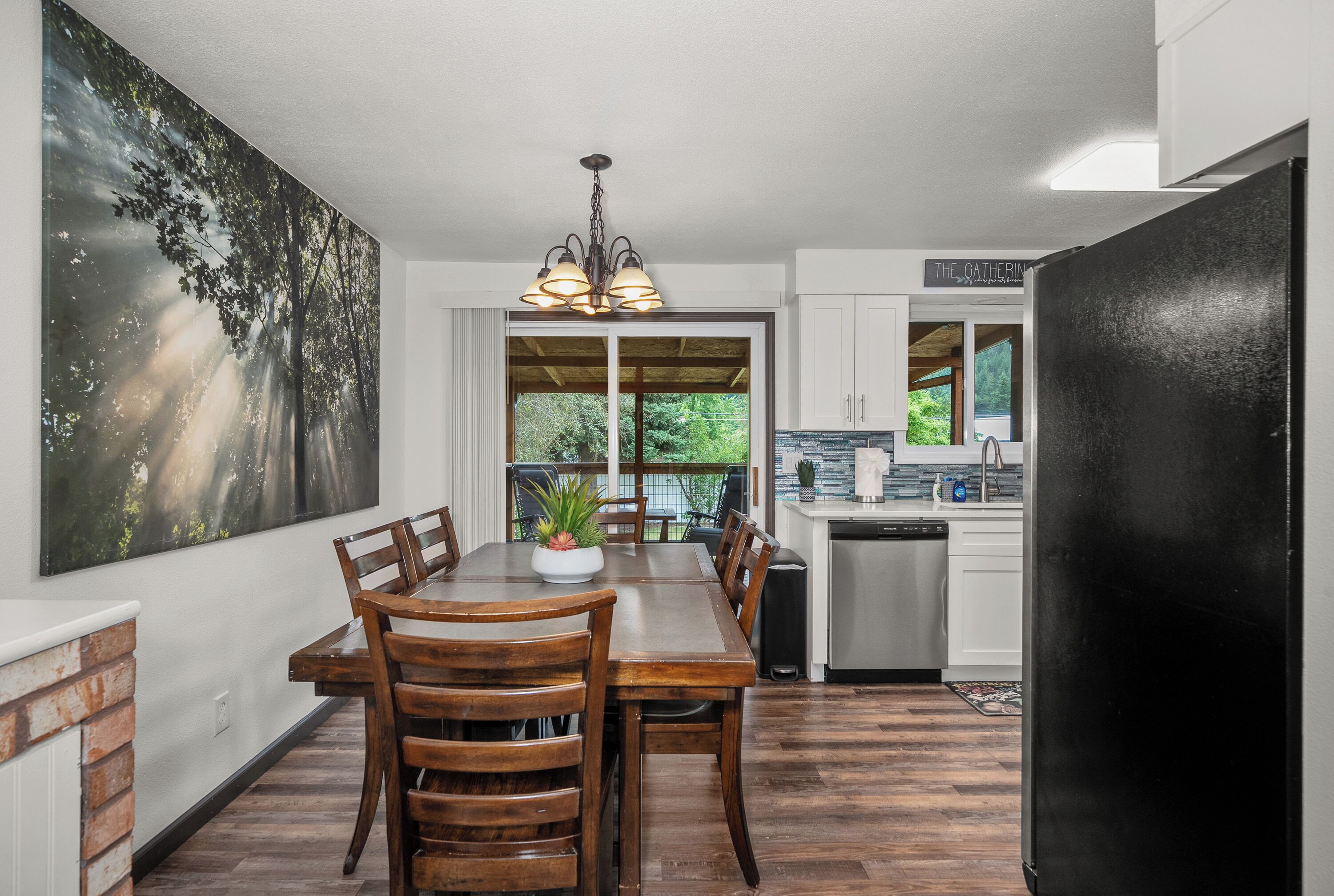 A modern kitchen with a dining area, featuring a large window, a chandelier, and a black refrigerator.