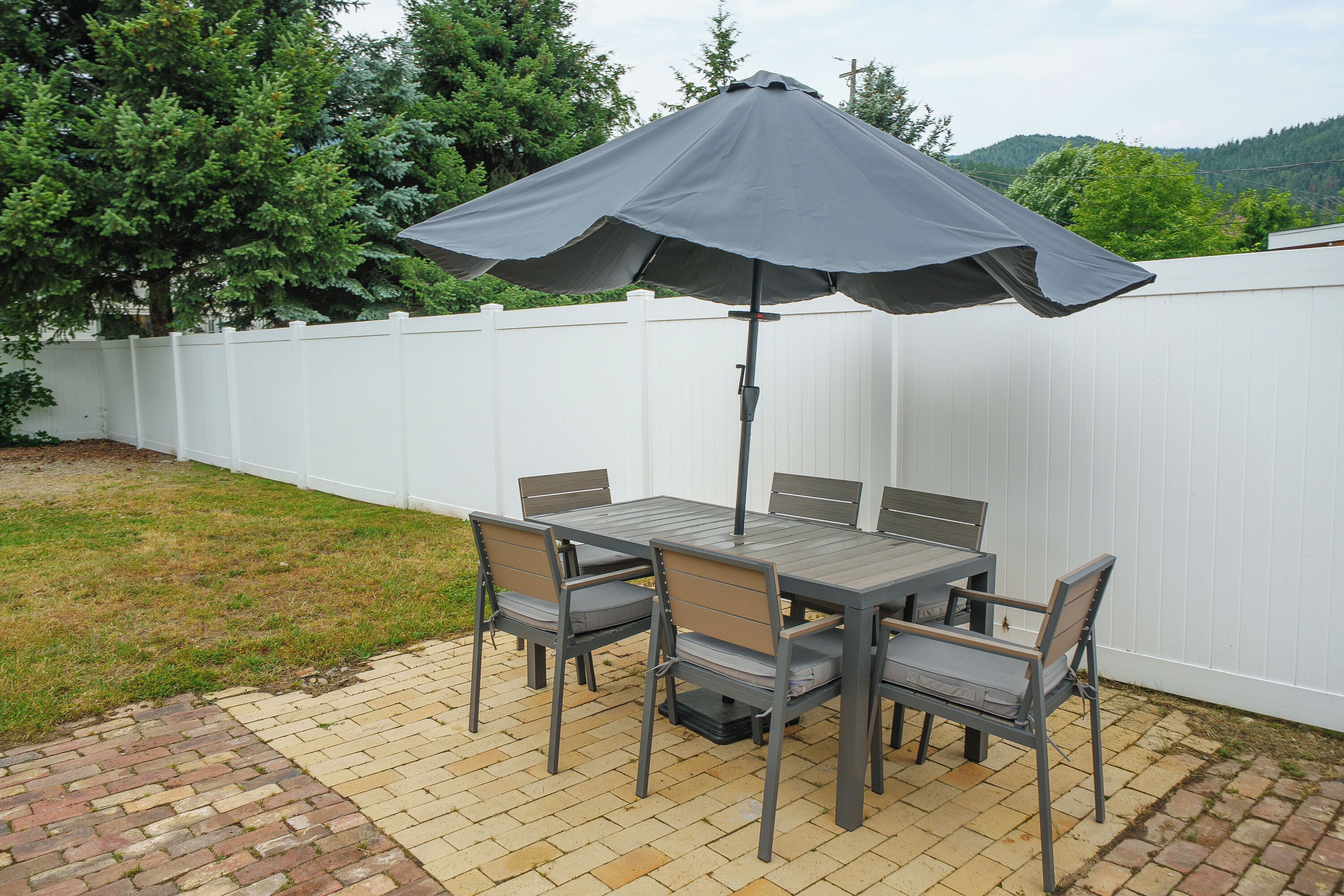 An outdoor patio with a table and chairs, a large umbrella, and a white fence.