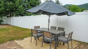 An outdoor patio with a table and chairs, a large umbrella, and a white fence.