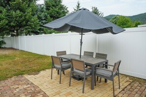 Une terrasse extérieure avec une table et des chaises, un grand parasol et une clôture blanche.