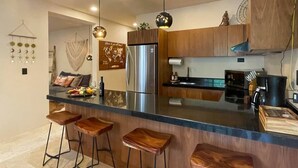Cozinha moderna com armários de madeira, geladeira de aço inoxidável e um espaço bar com banquetas.