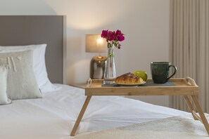 Een houten dienblad met een croissant, een groene kom en een bloevas op een bed.
