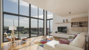 A spacious living room with large windows, a white sofa, a coffee table, and a TV on a wooden cabinet. - Pool, sun and sea view - Villa das Quebradas (Funchal)