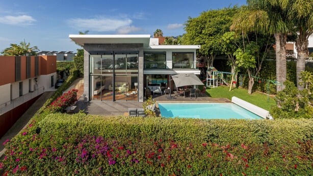 A modern house with a glass facade, a swimming pool, and a well-maintained garden. - Pool, sun and sea view - Villa das Quebradas (Funchal)