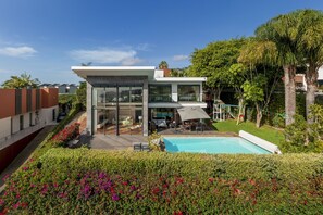 A modern house with a glass facade, a swimming pool, and a well-maintained garden. - Pool, sun and sea view - Villa das Quebradas (Funchal)