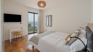 A bedroom with a bed, a desk, a chair, a television, and a large window with a view. - Pool, sun and sea view - Villa das Quebradas (Funchal)