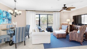 A spacious living room with a dining area, a sofa, and two patterned armchairs. A ceiling fan and a TV are visible. - 2 complimentary Bikes! Directly on 30A! Beach access across the street! (Santa Rosa Beach)