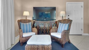 A living room with two wicker armchairs, a white ottoman, a flat-screen TV, and a cabinet with decorative glass doors. - 2 complimentary Bikes! Directly on 30A! Beach access across the street! (Santa Rosa Beach)