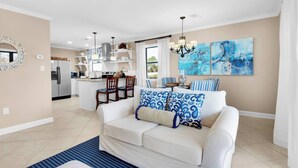 A modern living room with a white sofa, blue patterned cushions, a striped rug, and a dining area with striped chairs and a kitchen in the background. - 2 complimentary Bikes! Directly on 30A! Beach access across the street! (Santa Rosa Beach)
