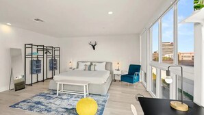 A modern bedroom with a large bed, a desk, a chair, and a view of the city through large windows. - Stylish 1BR Apt in Aventura★Pet Friendly★Pool★BBQ (miami)