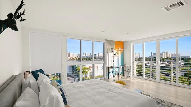 A modern bedroom with a large bed, a balcony with a city view, and a dining area with a table and chairs. - Stylish 1BR Apt in Aventura★Pet Friendly★Pool★BBQ (miami)