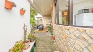 A narrow outdoor corridor with stone walls, potted plants, and outdoor furniture.