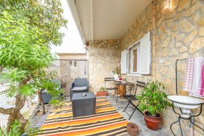 Une terrasse extérieure avec des murs en pierre, un tapis à rayures, des meubles en osier et des plantes en pot.