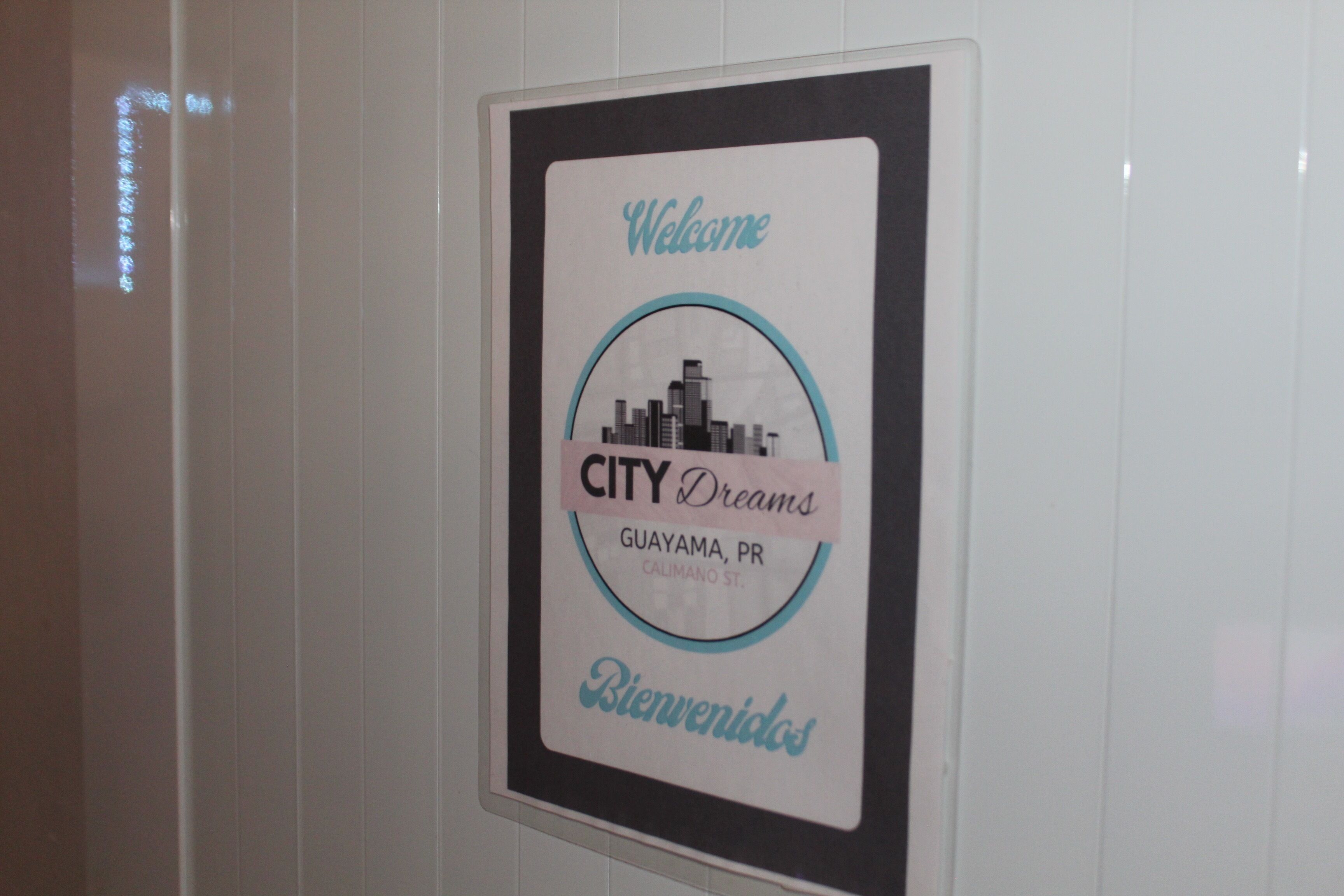 A welcome sign with a city skyline graphic, 'CITY Dreams' text, and location 'Guayama, PR' on a wall.
