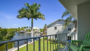 A balcony with a view of a water body, palm trees, and a house with a white exterior.