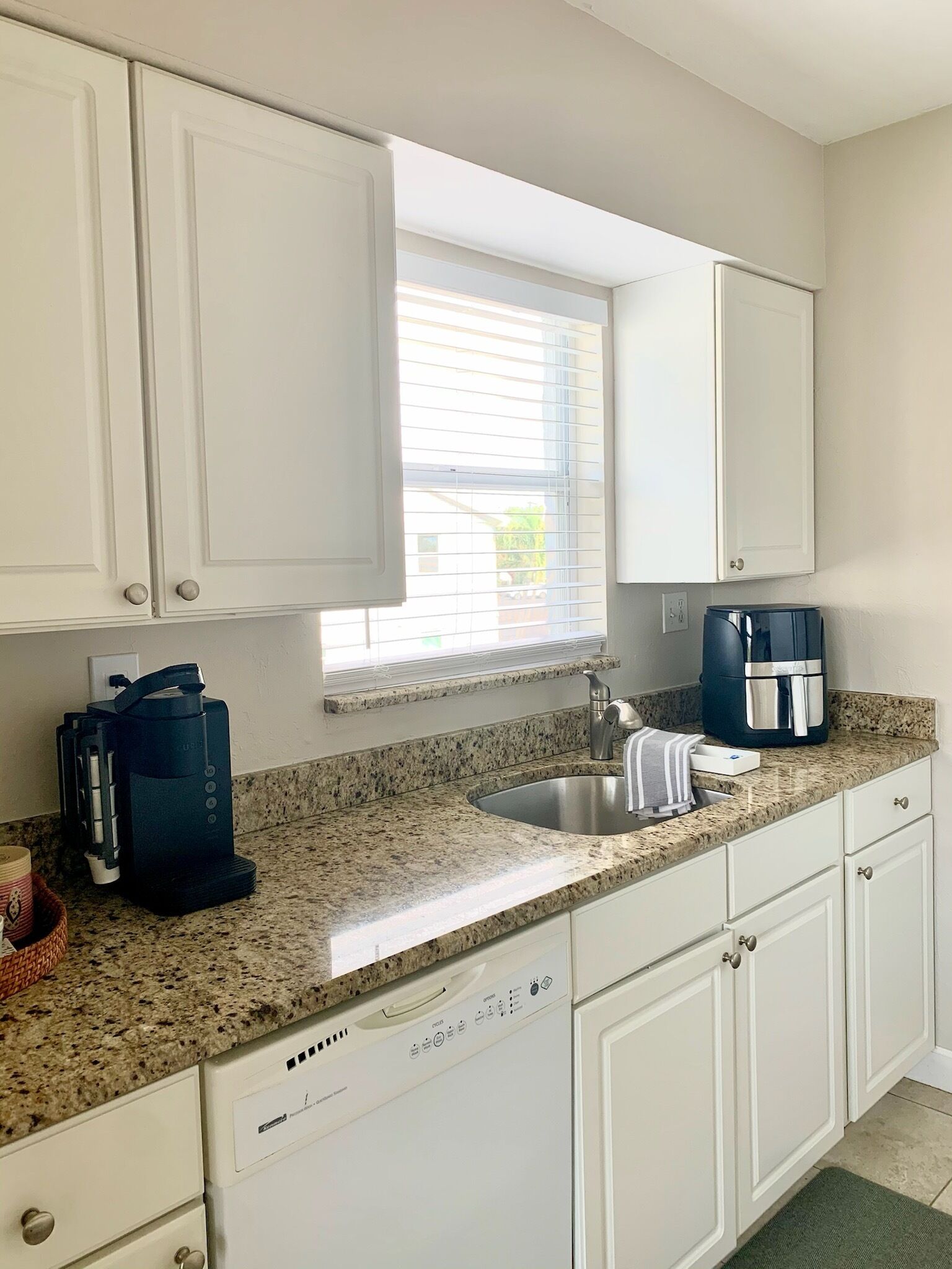 A kitchen with white cabinets, a granite countertop, a coffee maker, and a dishwasher.