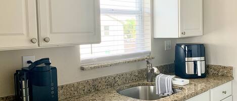 A kitchen with white cabinets, a granite countertop, a coffee maker, and a dishwasher.