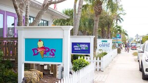 A sign for Anna General Maria Store and Island Charms, with a white picket fence and palm trees in the background.