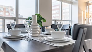 A dining table set with white bowls, wine glasses, and a white vase with green leaves.