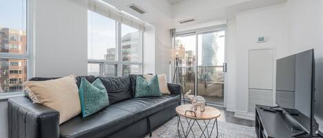 Una sala de estar moderna con un sofá de cuero negro, una mesa de centro redonda y un televisor sobre un mueble de madera.