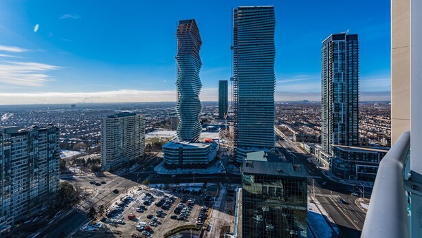 A high-rise building with a unique twisted architectural design, surrounded by other modern buildings and a parking lot.