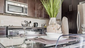 A modern kitchen with a glass dining table, white plates, and a vase with green plants.