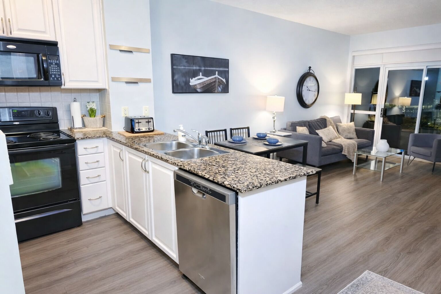 A modern kitchen with white cabinets, a built-in dishwasher, and a granite countertop.