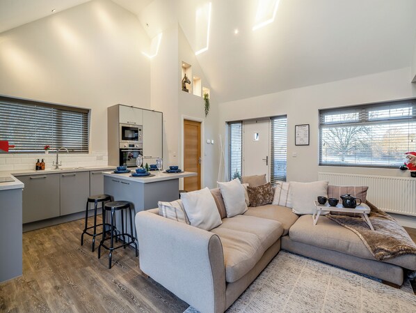 A modern kitchen with a central island, a dining area with a sofa, and a view of the outside through large windows.