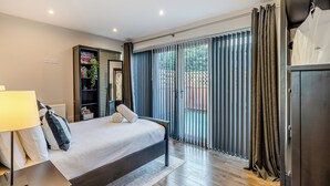 Een moderne slaapkamer met een bed, nachtkastje, kledingkast en een groot raam met gordijnen.