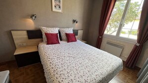 Un dormitori ordenat amb un llit, taules de nit, un quadre penjat a la paret i una finestra amb cortines.