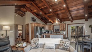 A spacious living room with a leather sofa, a dining area with a table and chairs, wooden cabinets, and a kitchen with modern appliances. - Moon Mountain Escape by Ruidoso Vacation Rentals (Ruidoso)