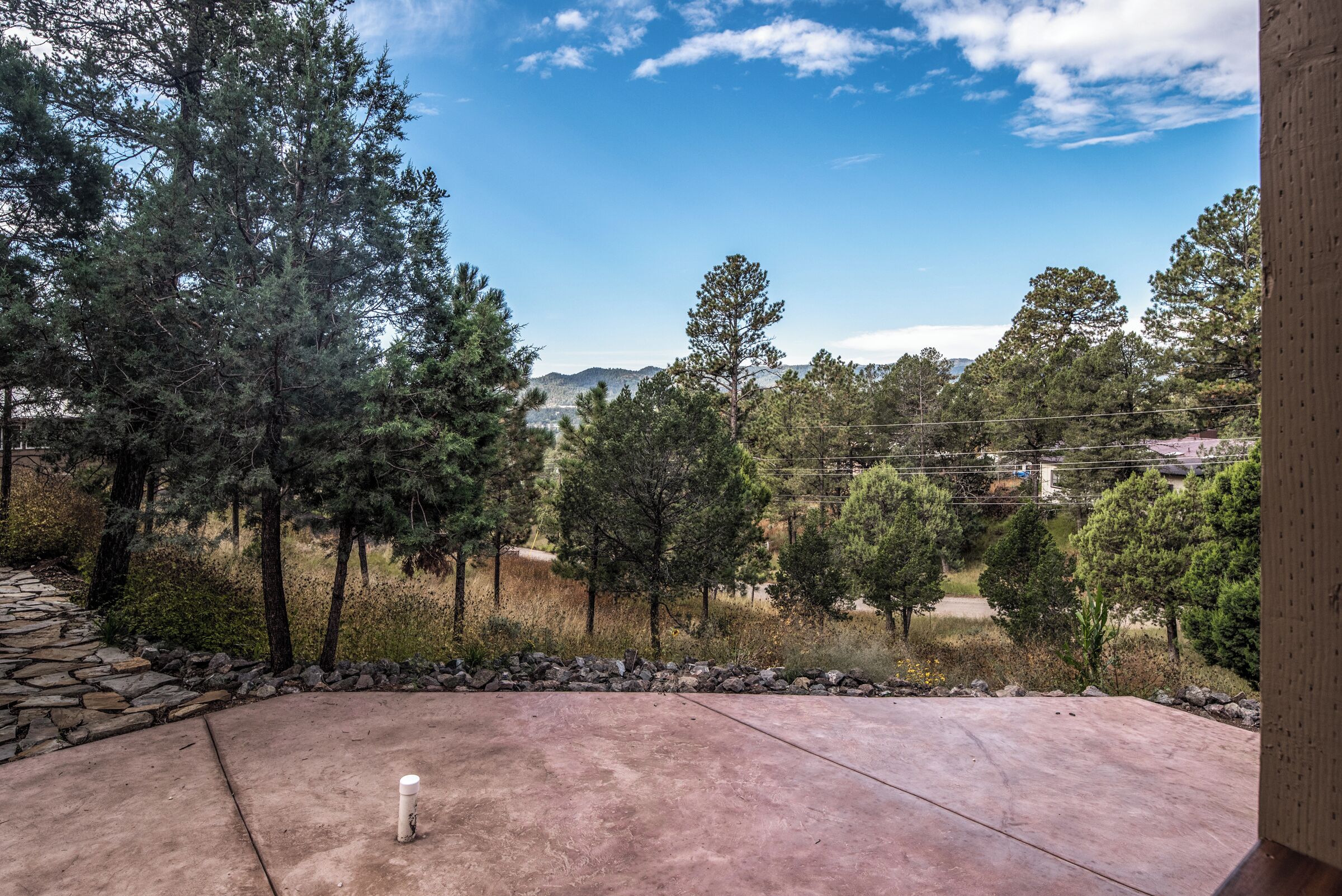 A patio with a stone wall and a view of a forest and distant hills.