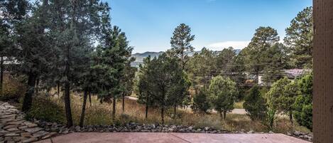 A patio with a stone wall and a view of a forest and distant hills.
