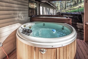 A wooden hot tub with a glass top, a wine glass, and a bottle of wine on the edge.