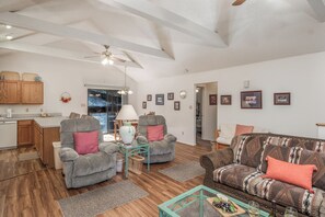 A spacious living room with a wooden floor, a sofa, two armchairs, a coffee table, and a ceiling fan. - Season 4 Art by Ruidoso Vacation Rentals (Ruidoso)