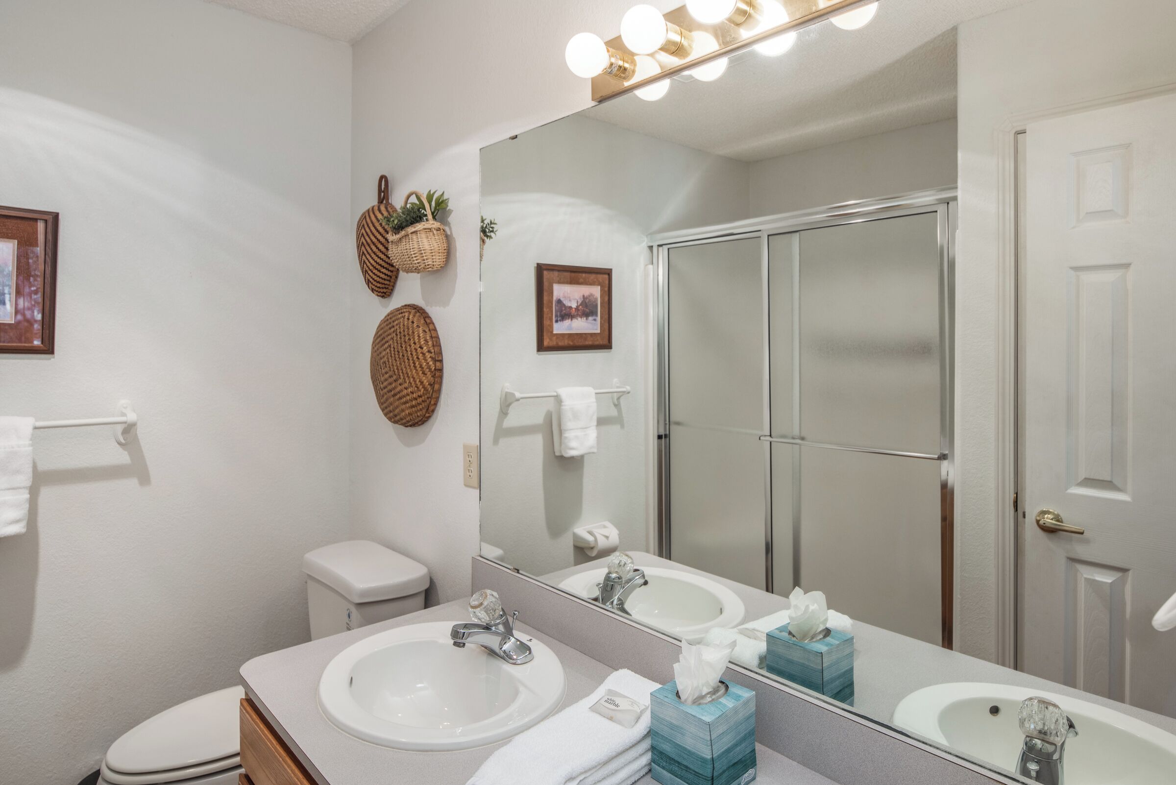 A bathroom with a large mirror, two sinks, a toilet, and a shower.