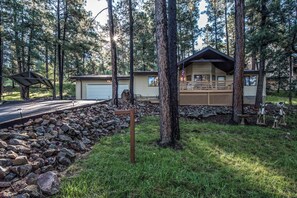 A cabin with a deck, surrounded by trees and a stone wall.