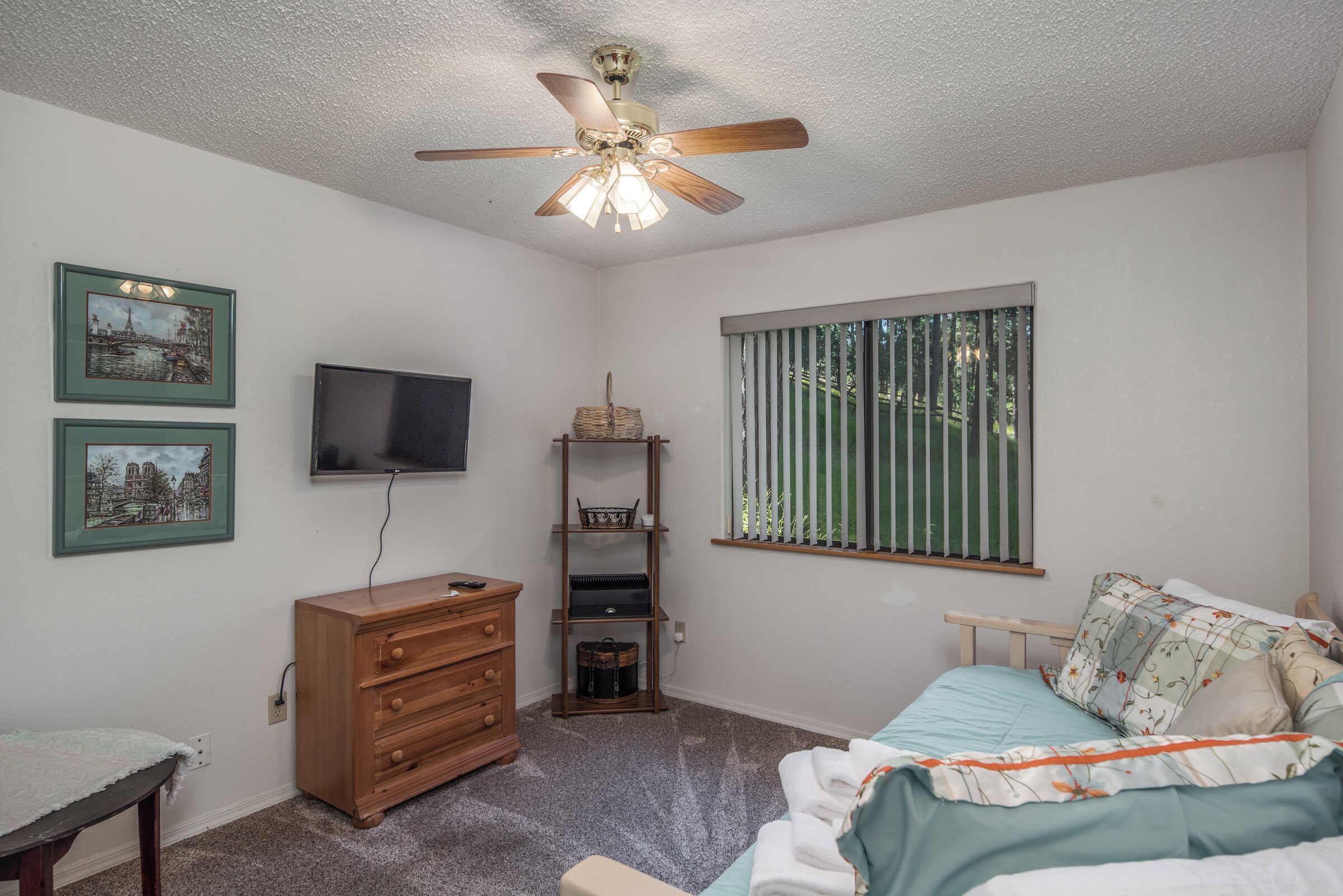 A bedroom with a bed, dresser, television, and a window with blinds.