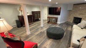 A living room with a red chair, a round ottoman, a beige sofa, a television, and a fireplace. - Cheerful 4 bedroom home with all the updates (Newtown)