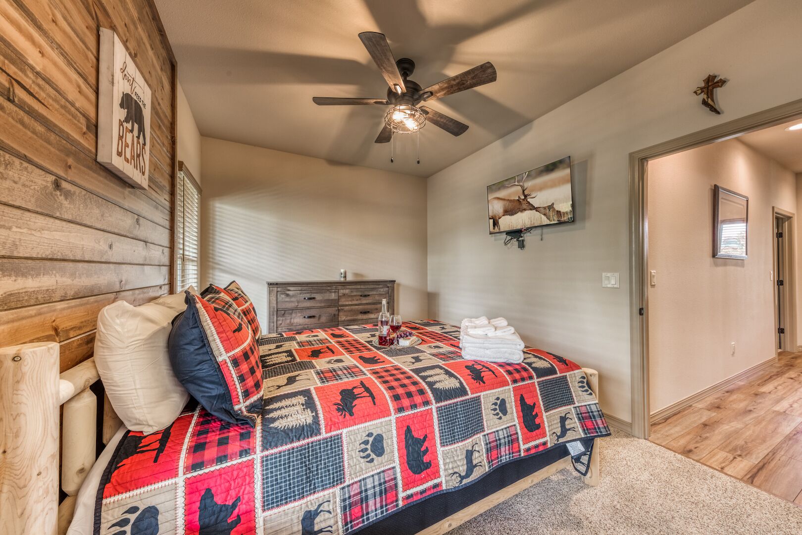 A bedroom with a wooden headboard, a quilted bedspread, a ceiling fan, a wooden dresser, and a framed picture on the wall.