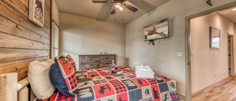 A bedroom with a wooden headboard, a quilted bedspread, a ceiling fan, a wooden dresser, and a framed picture on the wall.