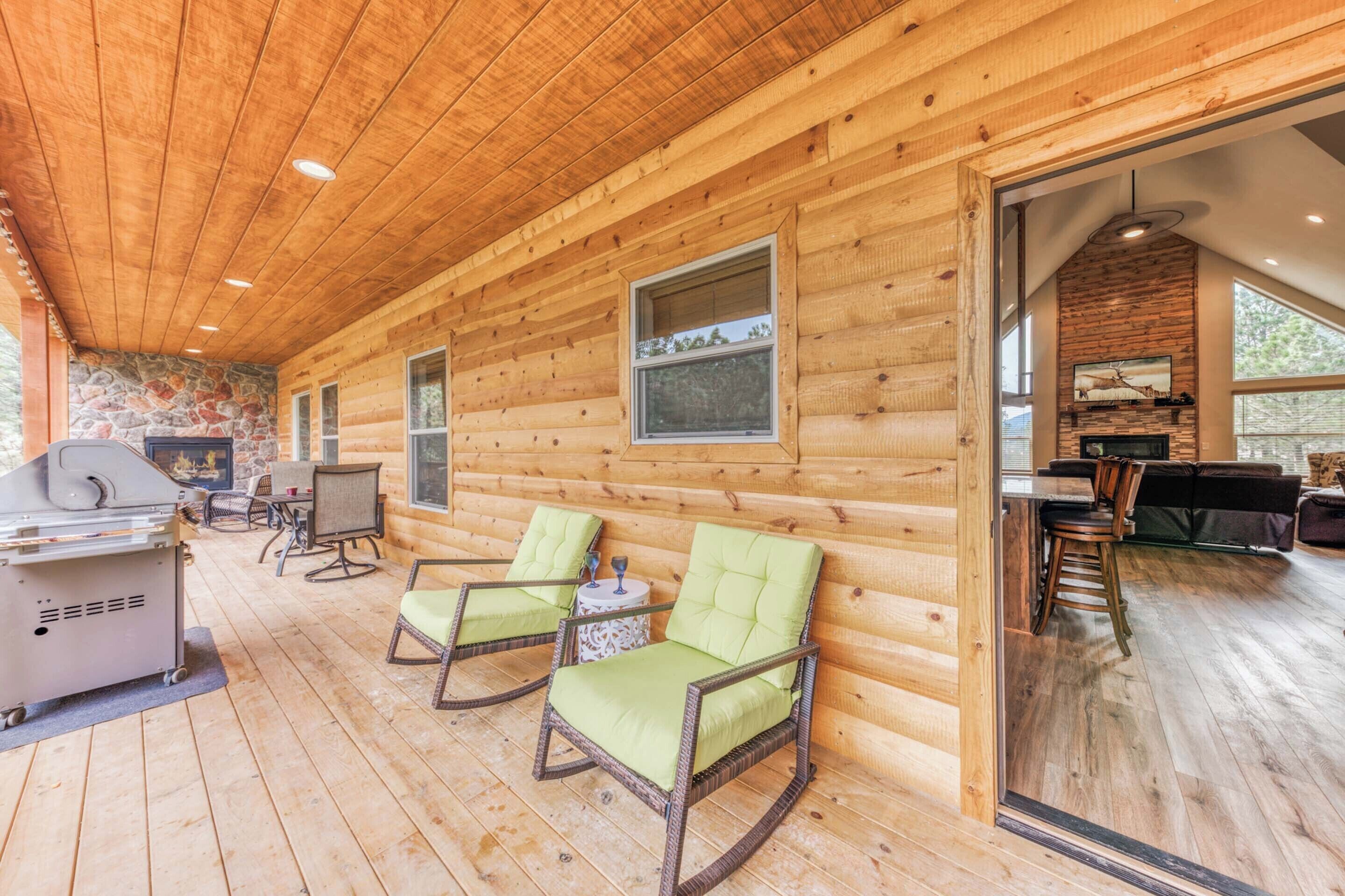 A wooden cabin with a covered porch, two rocking chairs, a grill, and a stone fireplace.