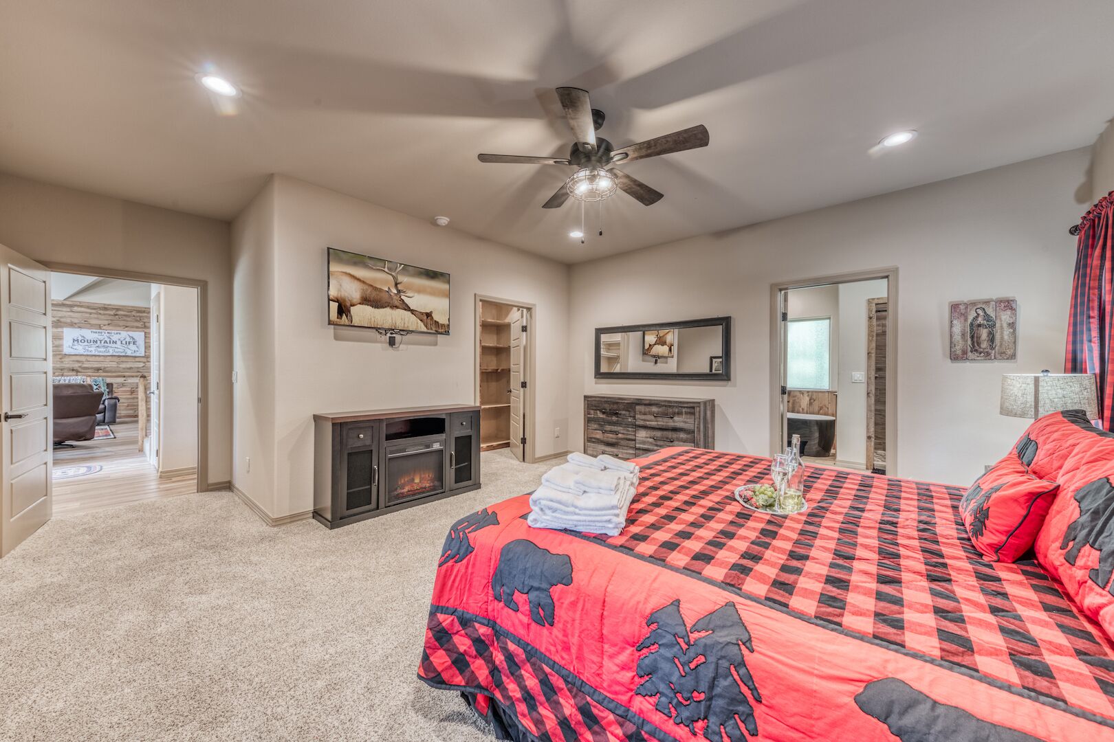 A bedroom with a large bed, a fireplace, a ceiling fan, and a door leading to another room.