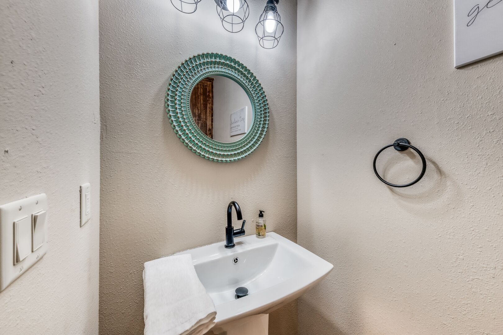Un baño con un lavabo blanco, un espejo con marco verde y una toalla colgada en la pared.