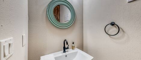 Un baño con un lavabo blanco, un espejo con marco verde y una toalla colgada en la pared.