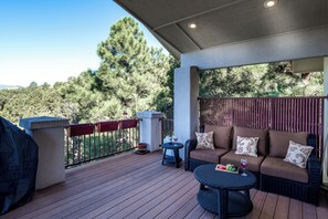 A covered outdoor deck with a sofa, a round table, and a grill. - Alto Grand View by Ruidoso Vacation Rentals (Alto)