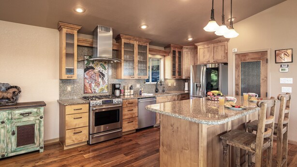 A kitchen with wooden cabinets, granite countertops, stainless steel appliances, and a central island with bar stools. - Alto Grand View by Ruidoso Vacation Rentals (Alto)